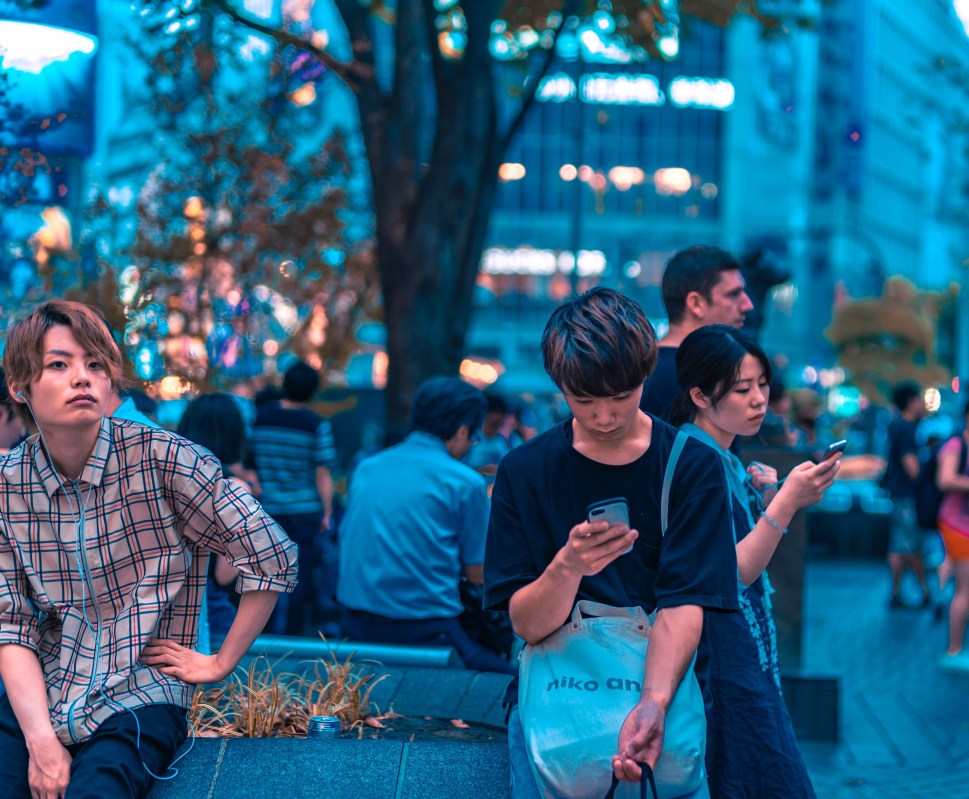 Asians in city setting looking at phone and wearing headphones.