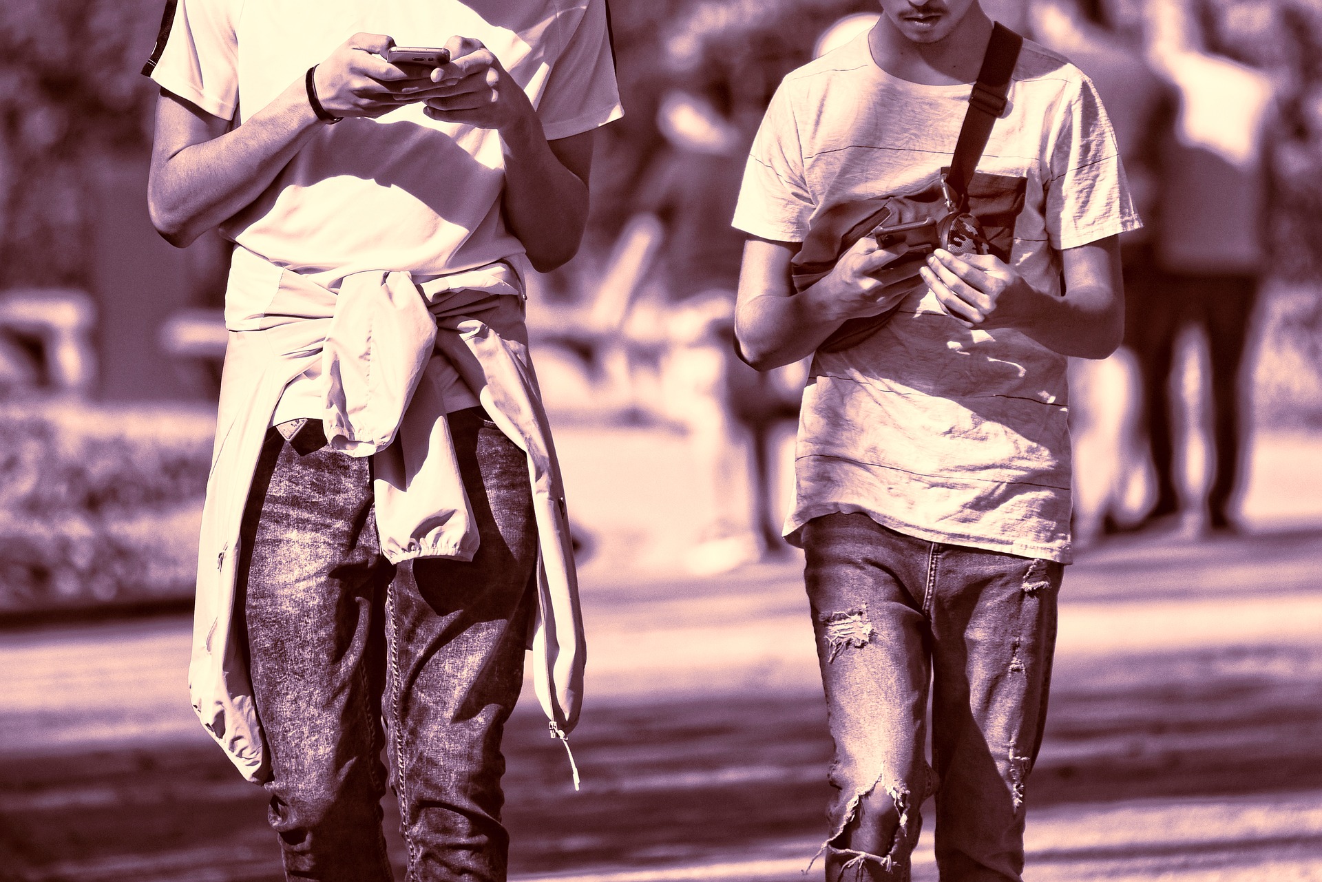 sepia photo of two guys in t-shirt and jeans walking while using phones