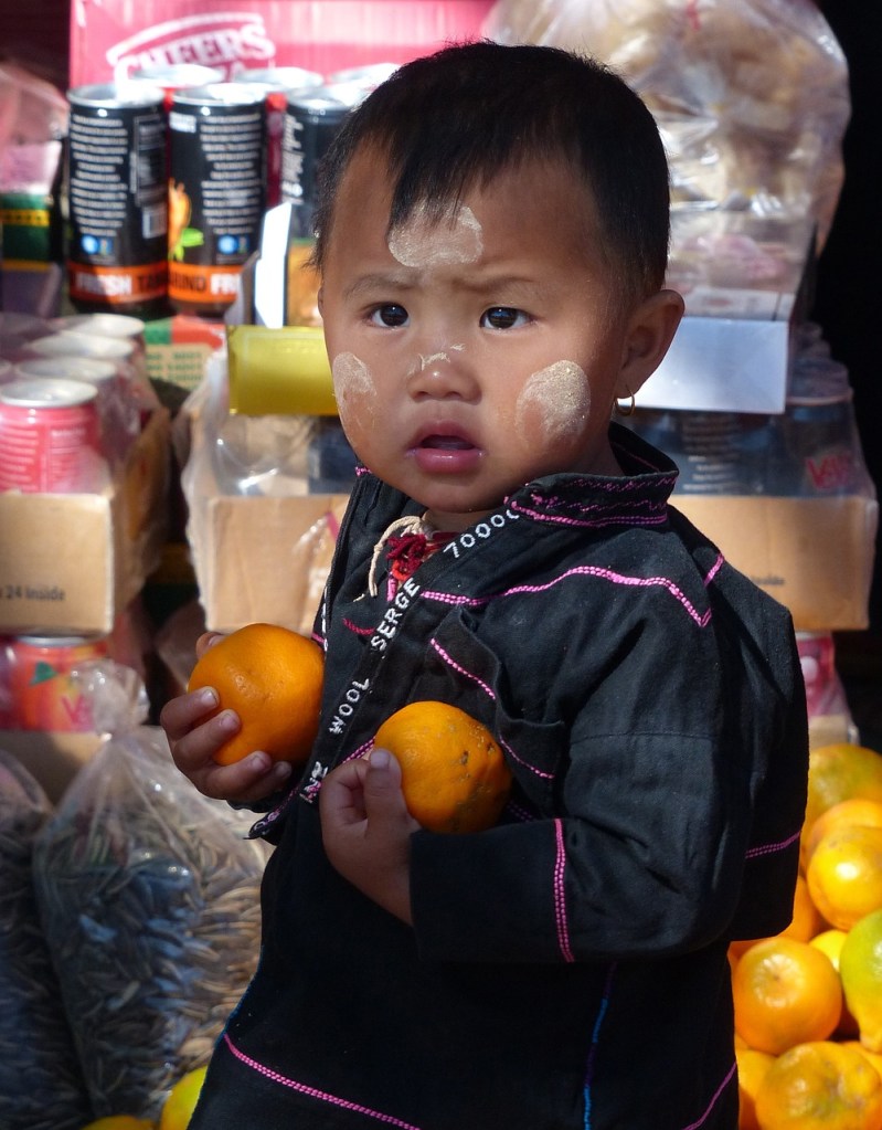 Asian child holding two tangerines, with flour-like smudges on his face