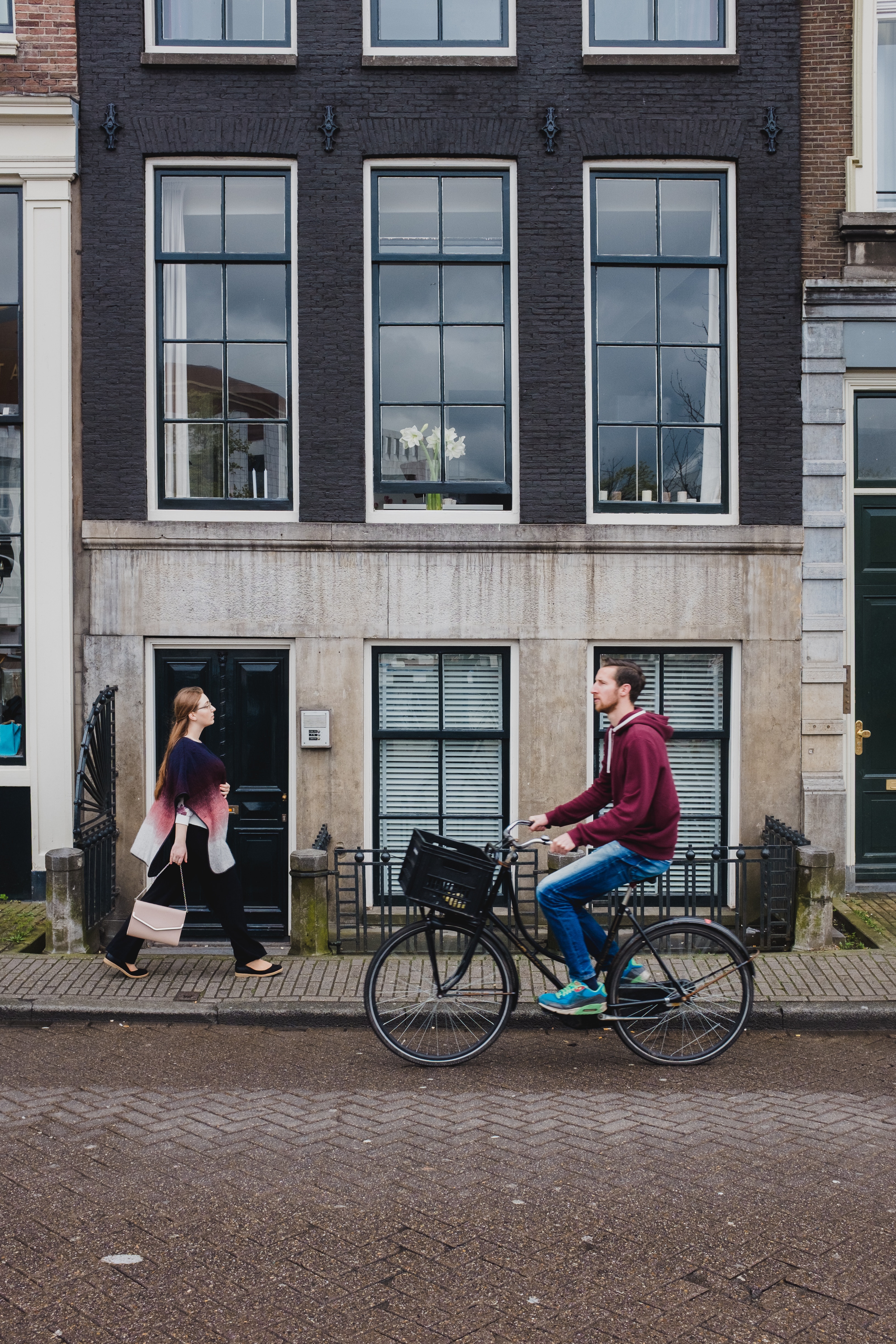 street view of multi-story building with large windows, a woman pedestrian and man cyclist in front